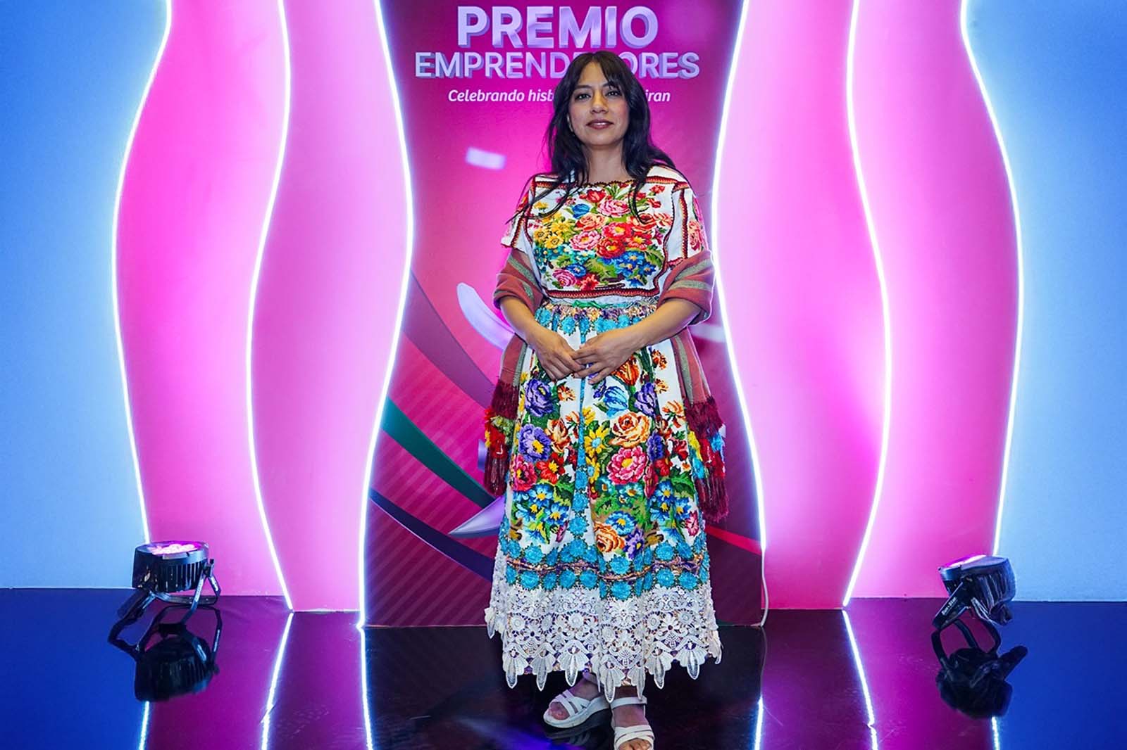 Martha Ramón en el escenario con vestido artesanal colorido en el Premio Emprendedores 2024 Yastás.